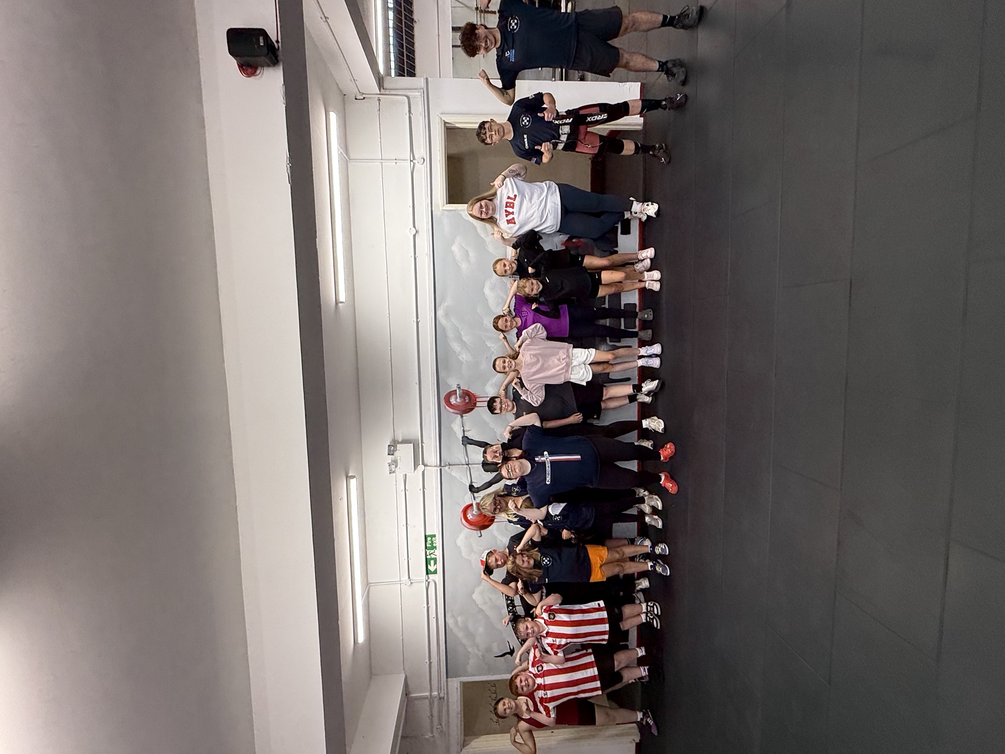 A large group of young members and their coaches lined up across the gym, arms raised